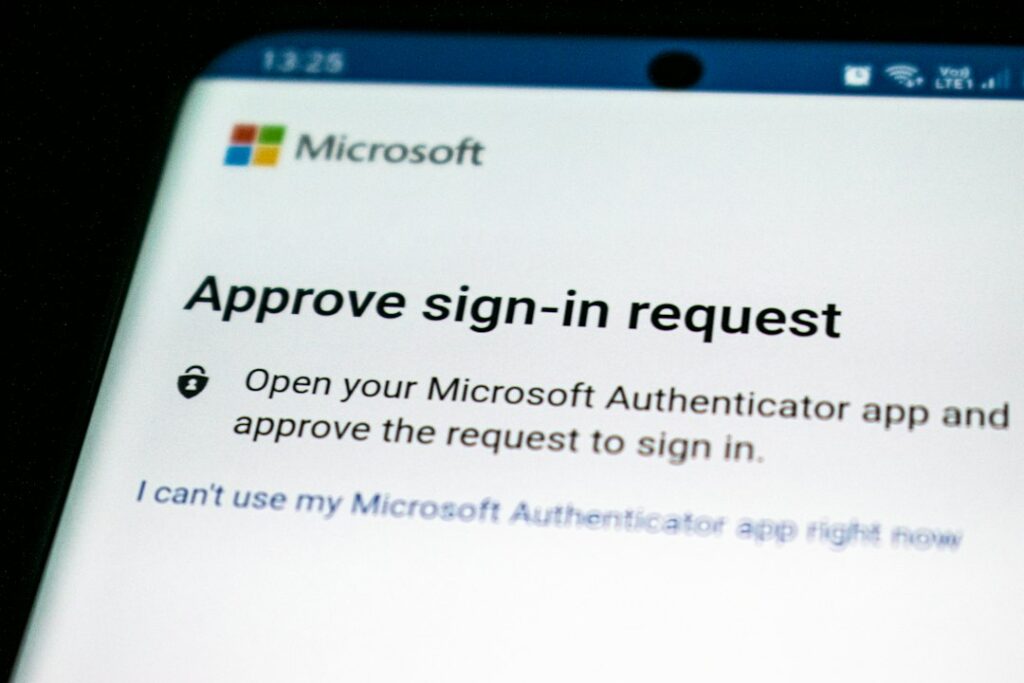 A person enters a verification code on a laptop while holding a smartphone with an authentication app.